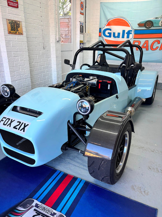 Light blue open-wheeled race car in a garage with Gulf Racing branding in the background.